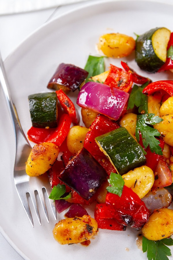 a white plate with veggies and gnocchi on it and a fork to the left.