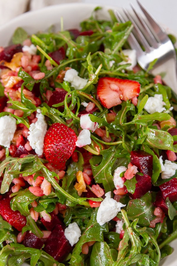 close up on a salad with arugula strawberries and beets and a fork in the upper right of the bowl.