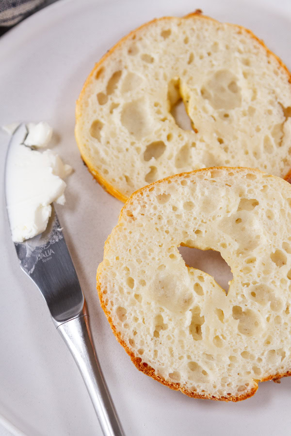 a cut open bagel with a knife covered in cream cheese next to it.