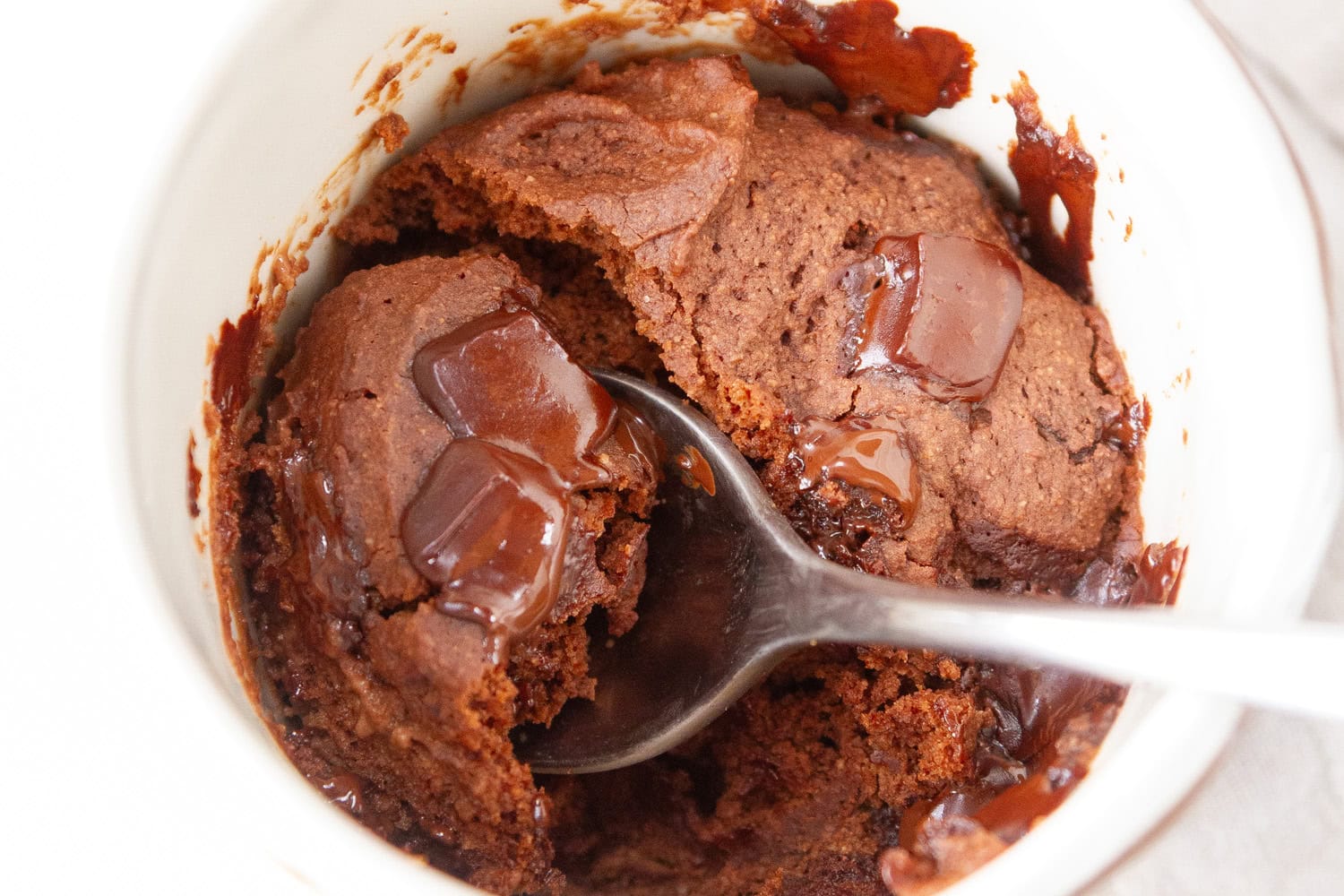 looking down into a mug with chocolate cake and a spoon in it.
