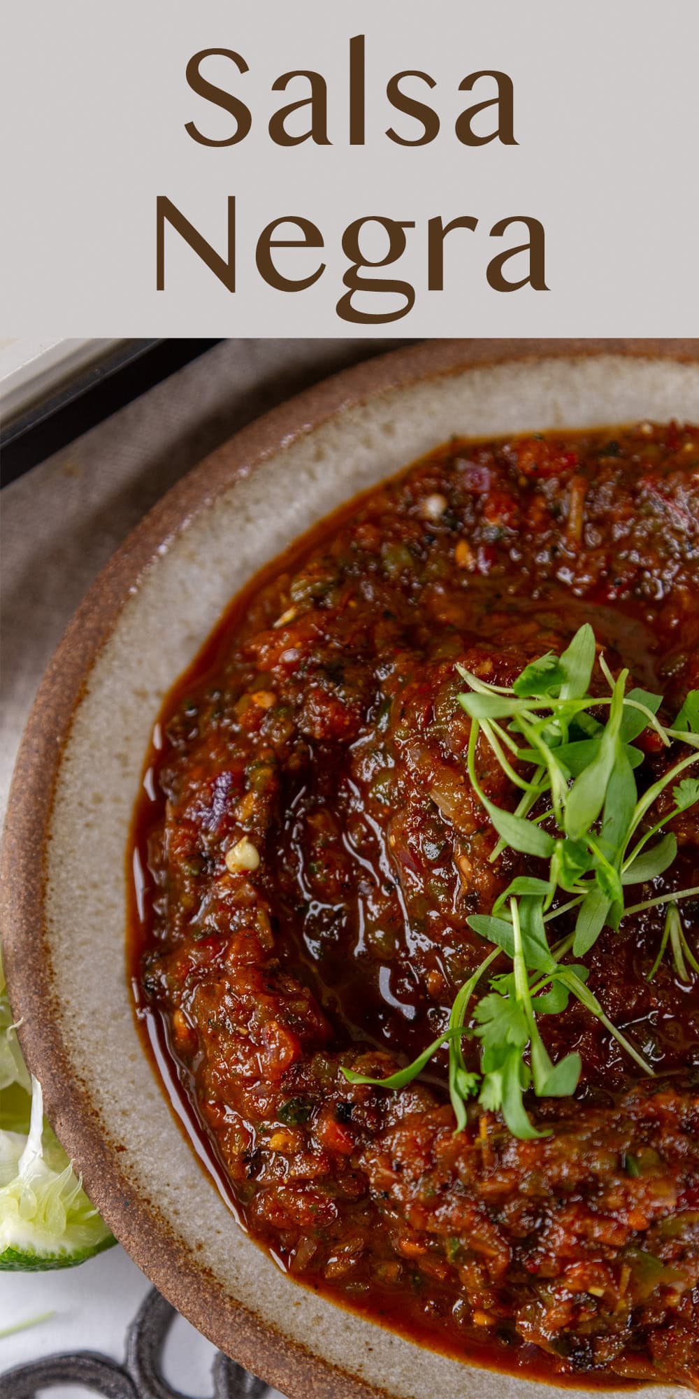 a bowl filled with dark red salsa, salsa negra, that's garnished with cilantro sprouts.