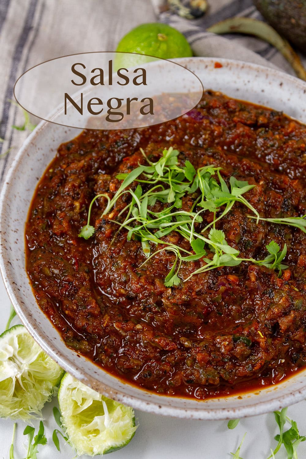 a white bowl filled with black salsa topped with cilantro sprouts, squeezed limes to the lower left.