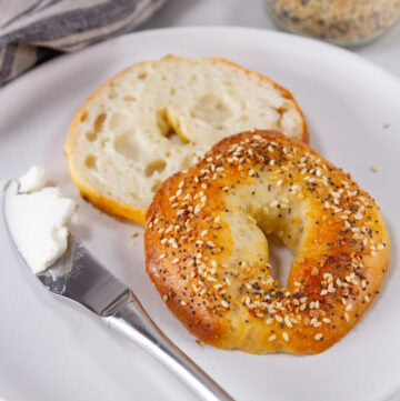 an everything bagel cut open with a cream cheese covered knife to the left.