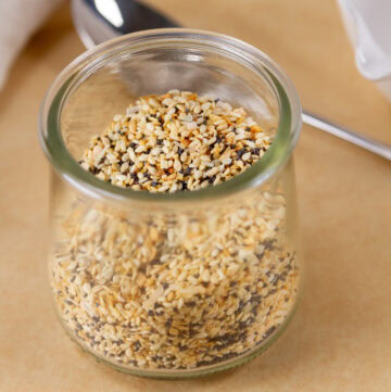 a glass jar with seasoning mix in it with a spoon in the background.