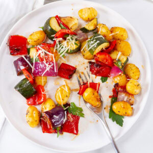 looking down on a white plate filled with colorful roasted veggies and a fork in the middle.