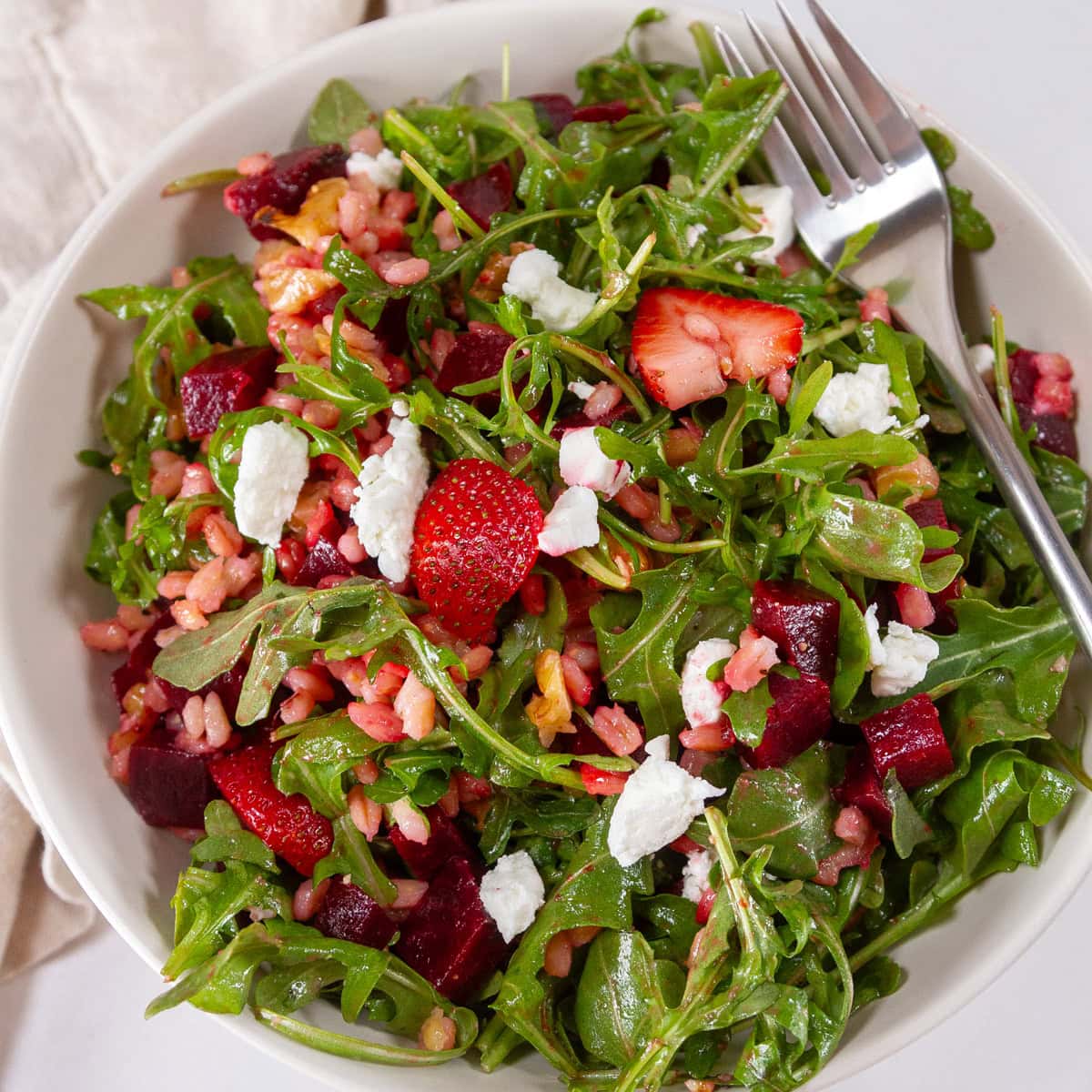 looking down into a white bowl filled with a colorful salad and a fork on the right side.