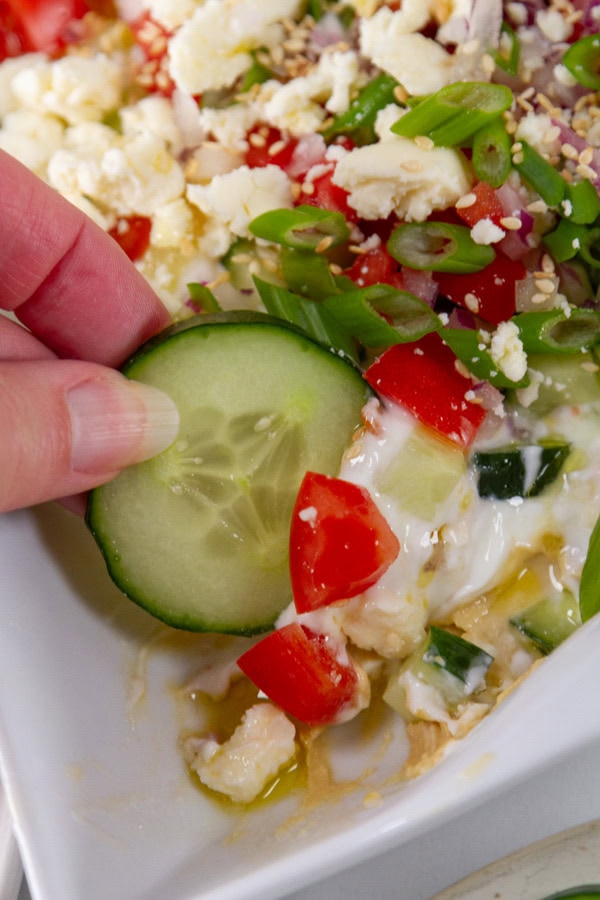 dipping a cucumber slice into 7 layer dip.
