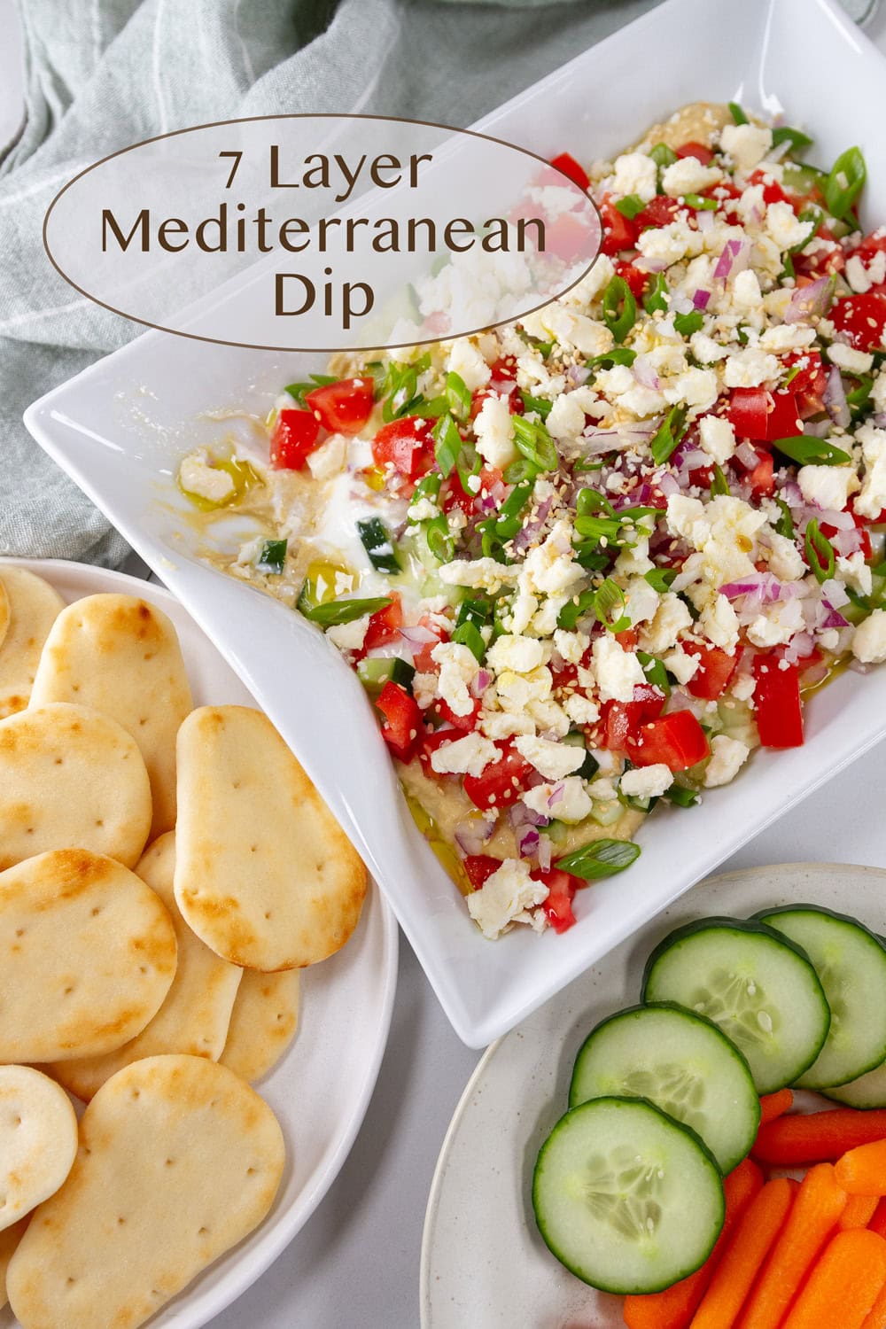a platter of layered dip served with naan and veggies on the side.