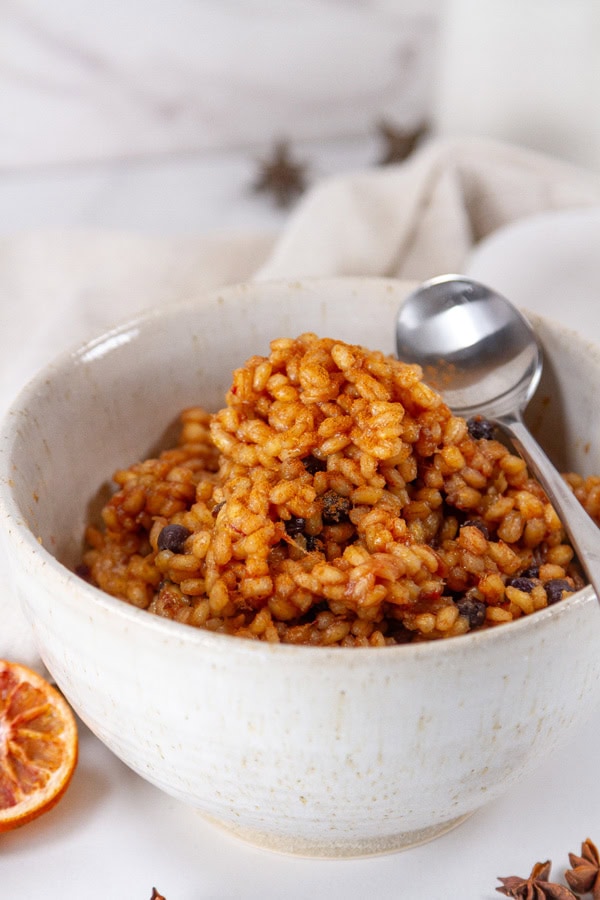 a white bowl filled with cooked barley and a spoon.