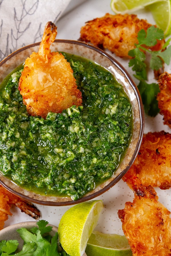 coconut shrimp dipped in cilantro pesto with lime wedges around it.