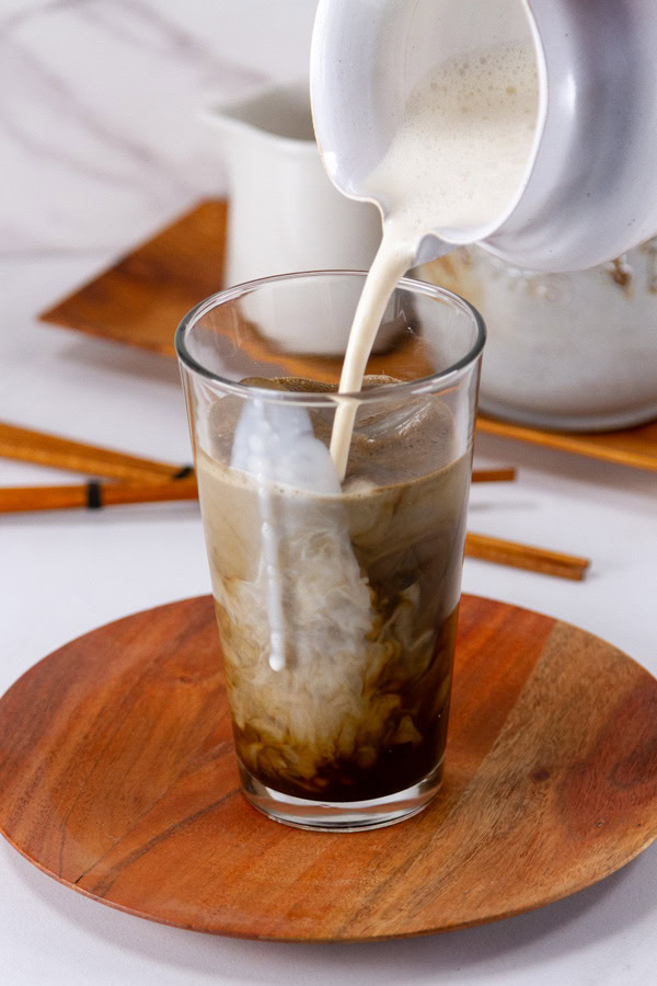 pouring milk into an iced latte on a wooden plate.
