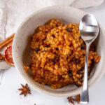 square crop looking down into a bowl of cooked barley with a spoon spices around the bowl.