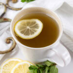 square crop of a white mug with tea in it, mint sprigs and lemon slices around.