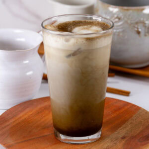 a glass of tea latte on a wooden plate with ceramic dishes behind it.
