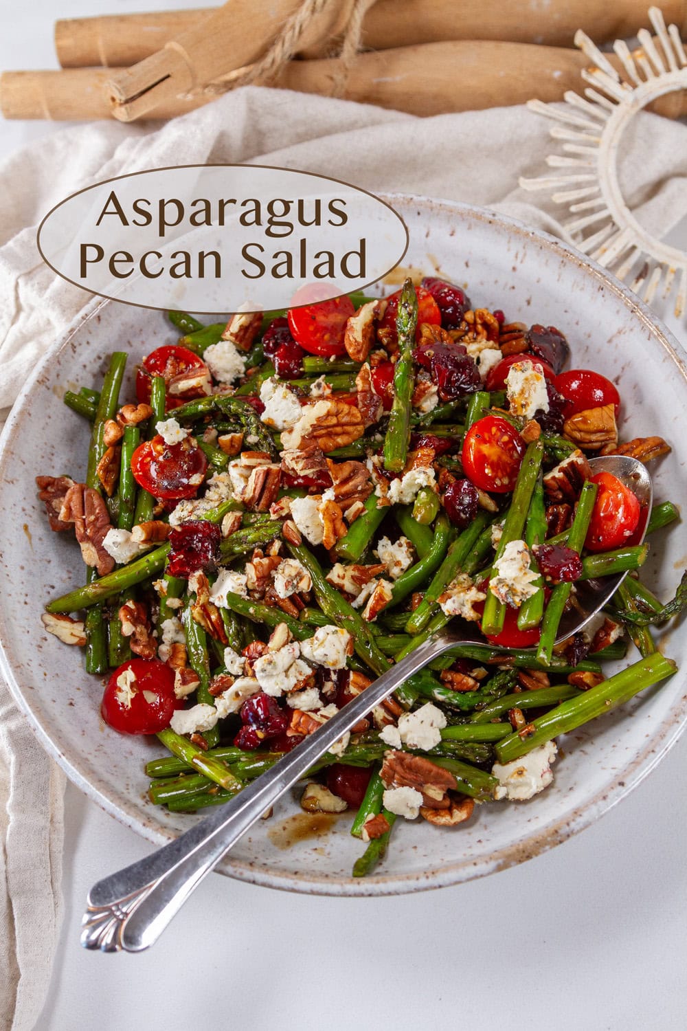 A white bowl with asparagus side dish with tomatoes and goat cheese on a white background with some wooden pieces in the background.