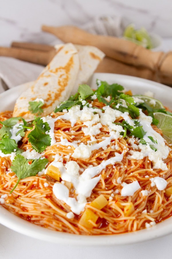 a bowl full of noodle soup with a tortilla on the side.