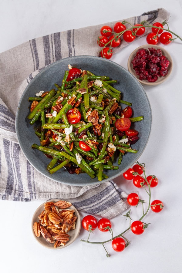 a large blue bowl with salad in it, small bowls of pecans and cranberries on the sides, and some cherry tomatoes around.