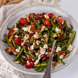 square crop of a white bowl filled with asparagus salad and a spoon in it.