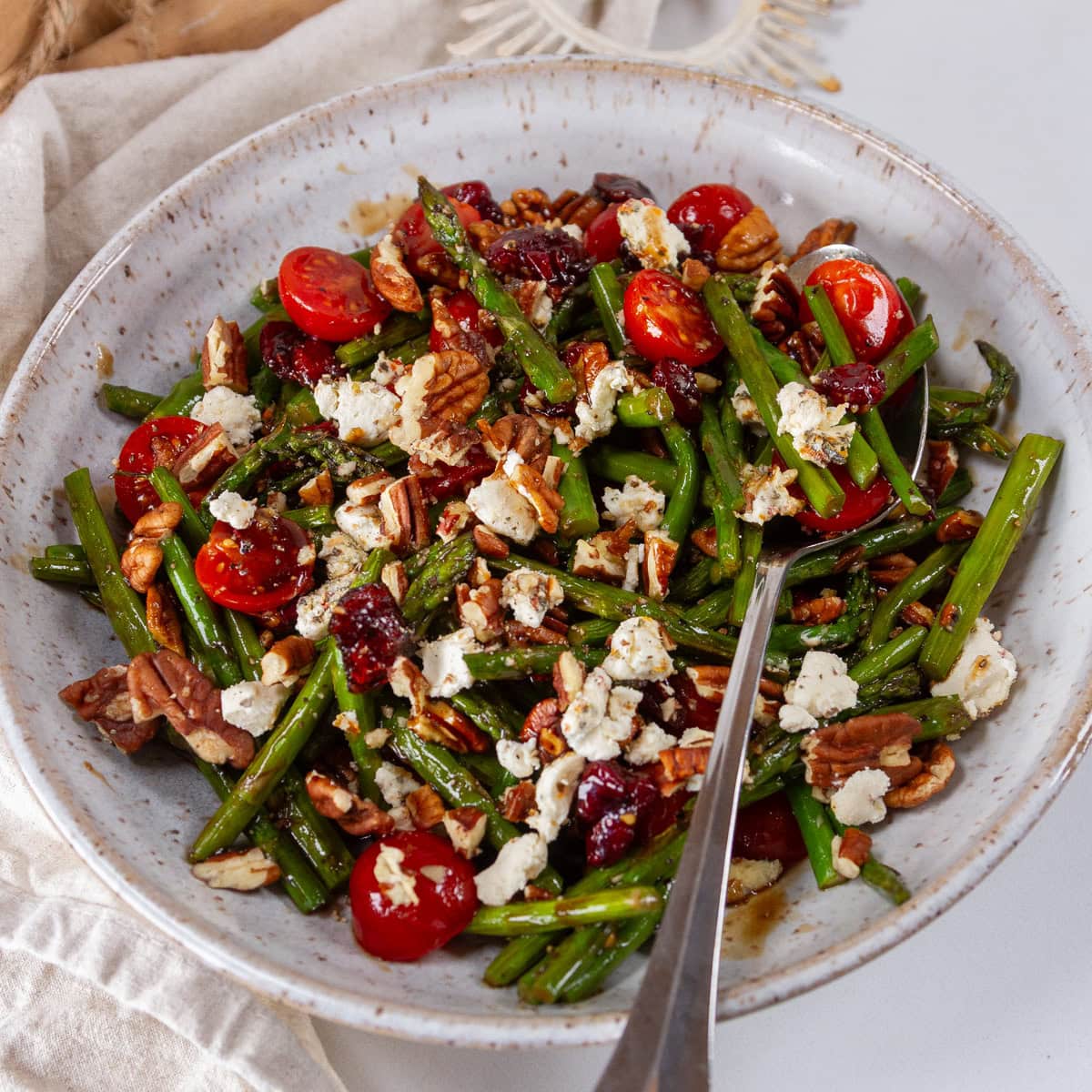 square crop of a white bowl filled with asparagus salad and a spoon in it.
