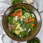 square crop looking down into a chimichurri bowl with veggies, cheese, salmon and a fork to the left.