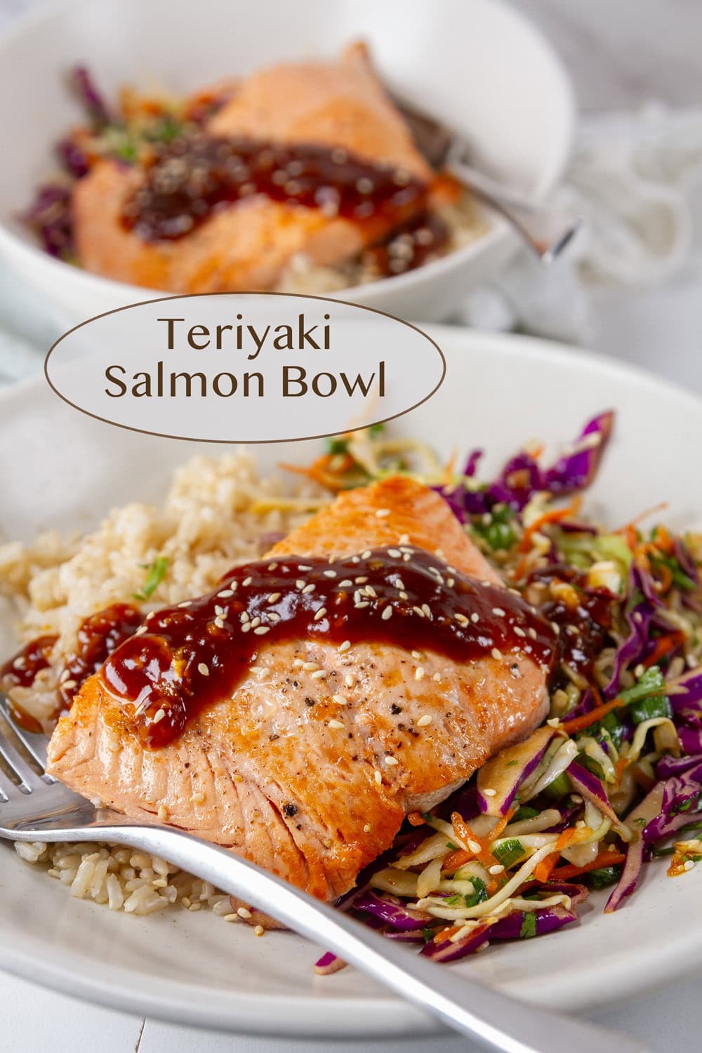 two teriyaki salmon bowls with seared salmon, cabbage slaw, and brown rice with forks in the bowls.