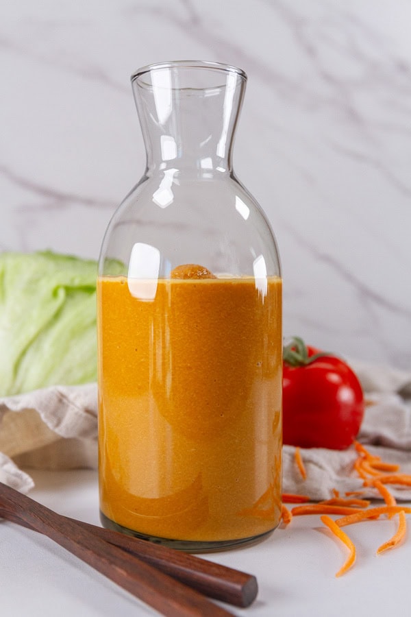 a bottle of salad dressing with chopsticks, a head of lettuce, and a tomato around it.