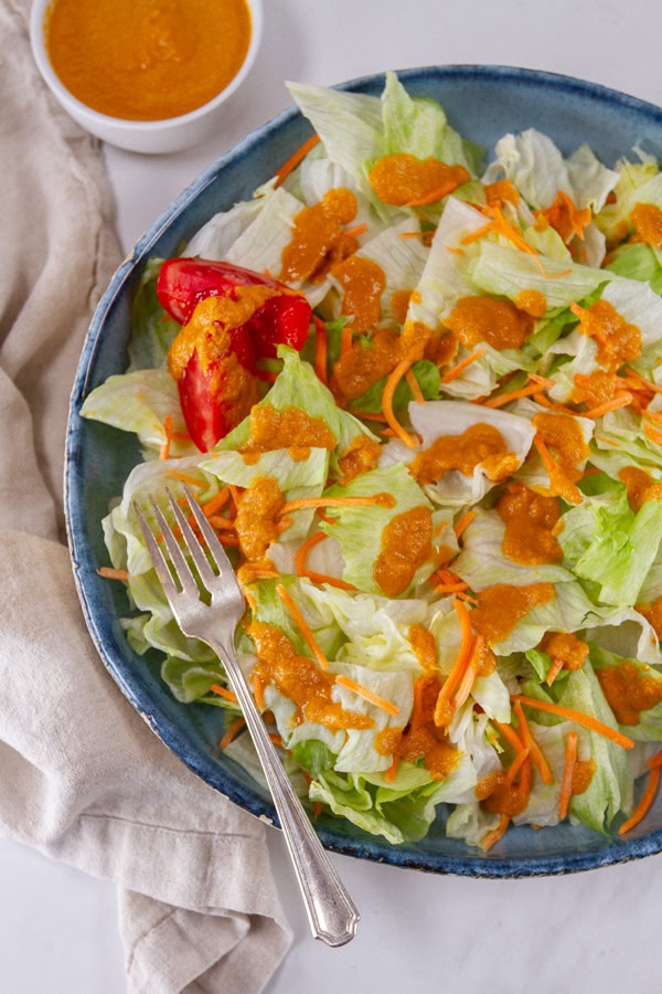 a large blue bowl filled with salad and a fork in the bowl, a small bowl of dressing in the upper left.