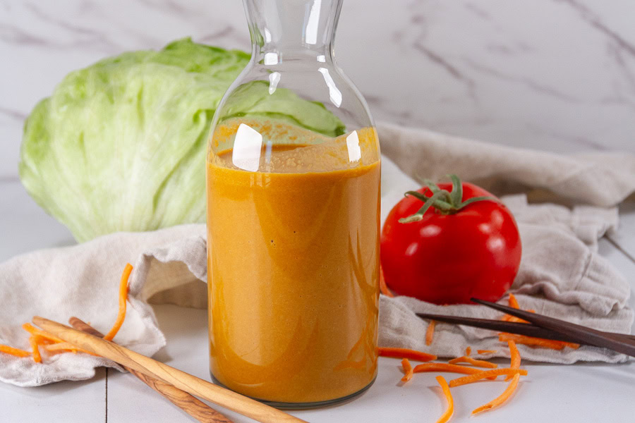 a bottle of salad dressing in front of a head of lettuce and a tomato.