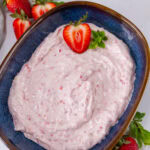 square crop of a blue bowl filled with pink strawberry cream cheese and some fresh strawberries.