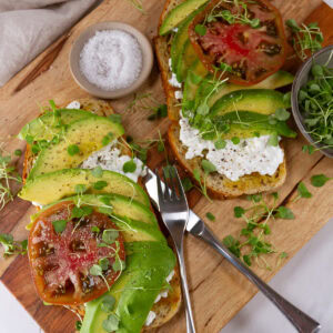 square crop looking down on two pieces of avocado toast on a wooden cutting board.