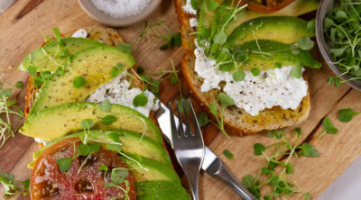 square crop looking down on two pieces of avocado toast on a wooden cutting board.