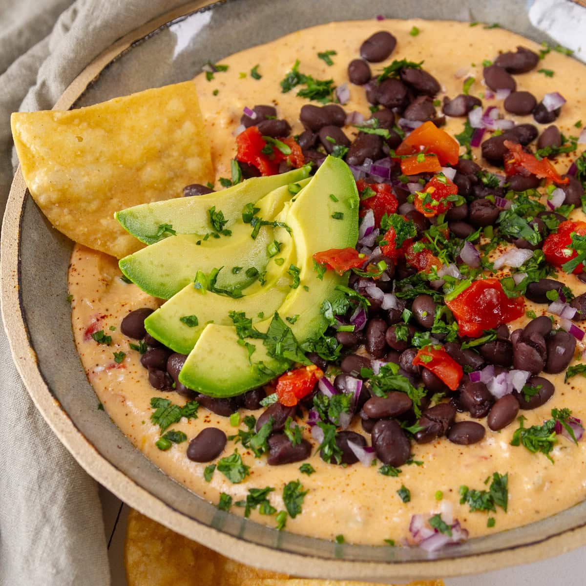 a bowl filled with cottage cheese queso and loated with black beans, tomatoes, cilantro, and avocado.