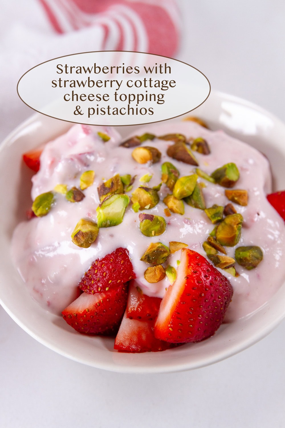 fresh strawberries in a white bowl topped with cottage cheese strawberry sauce and pistachios.