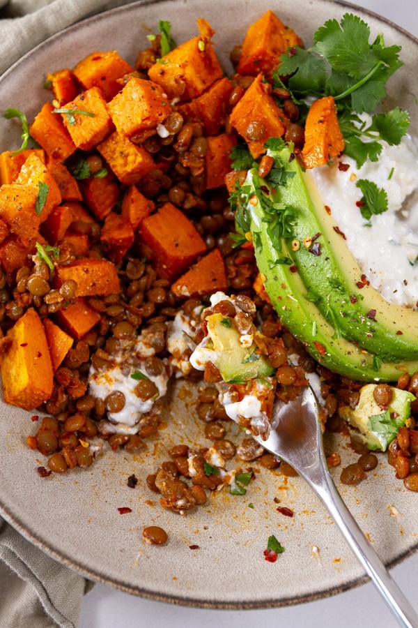 A bowl of lentils, sweet potatoes, avocado, and cottage cheese being partially eaten.