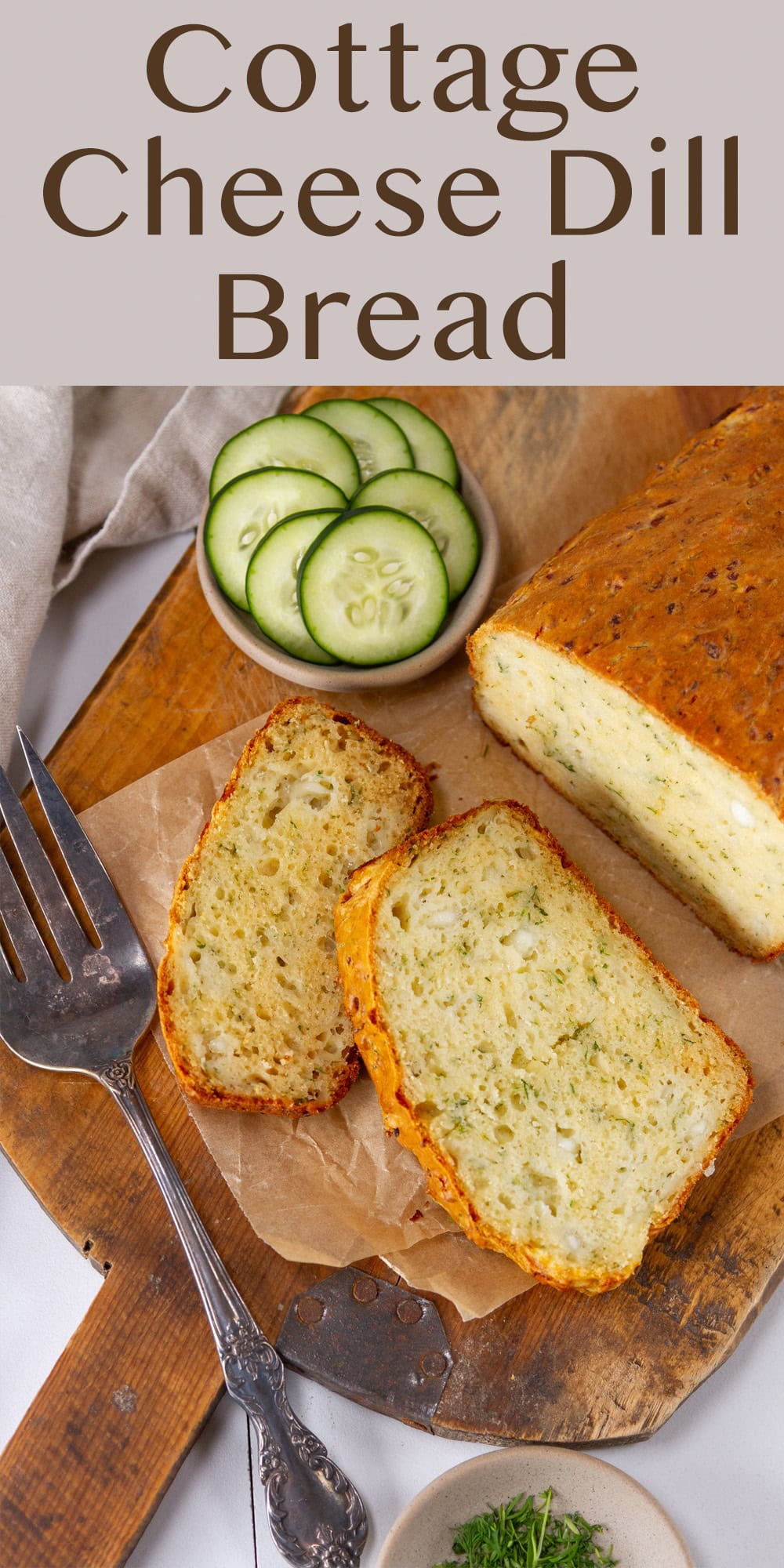 a loaf of bread with a bowl of cucumber slices on a wooden cutting board.