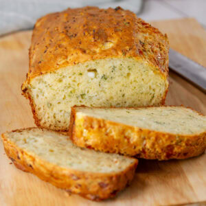 square crop of a sliced loaf of bread on a cutting board with a bread knife to the right.