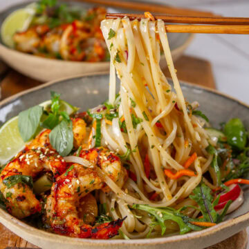 square crop of chopsticks pulling up noodles out of a bowl with shrimp and salad in it.