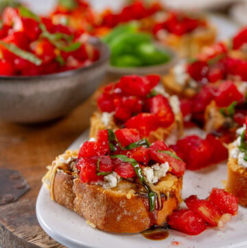 square crop of tomato bruschetta appetizers on a tray with a small bowl of chopped tomatoes next to the tray.