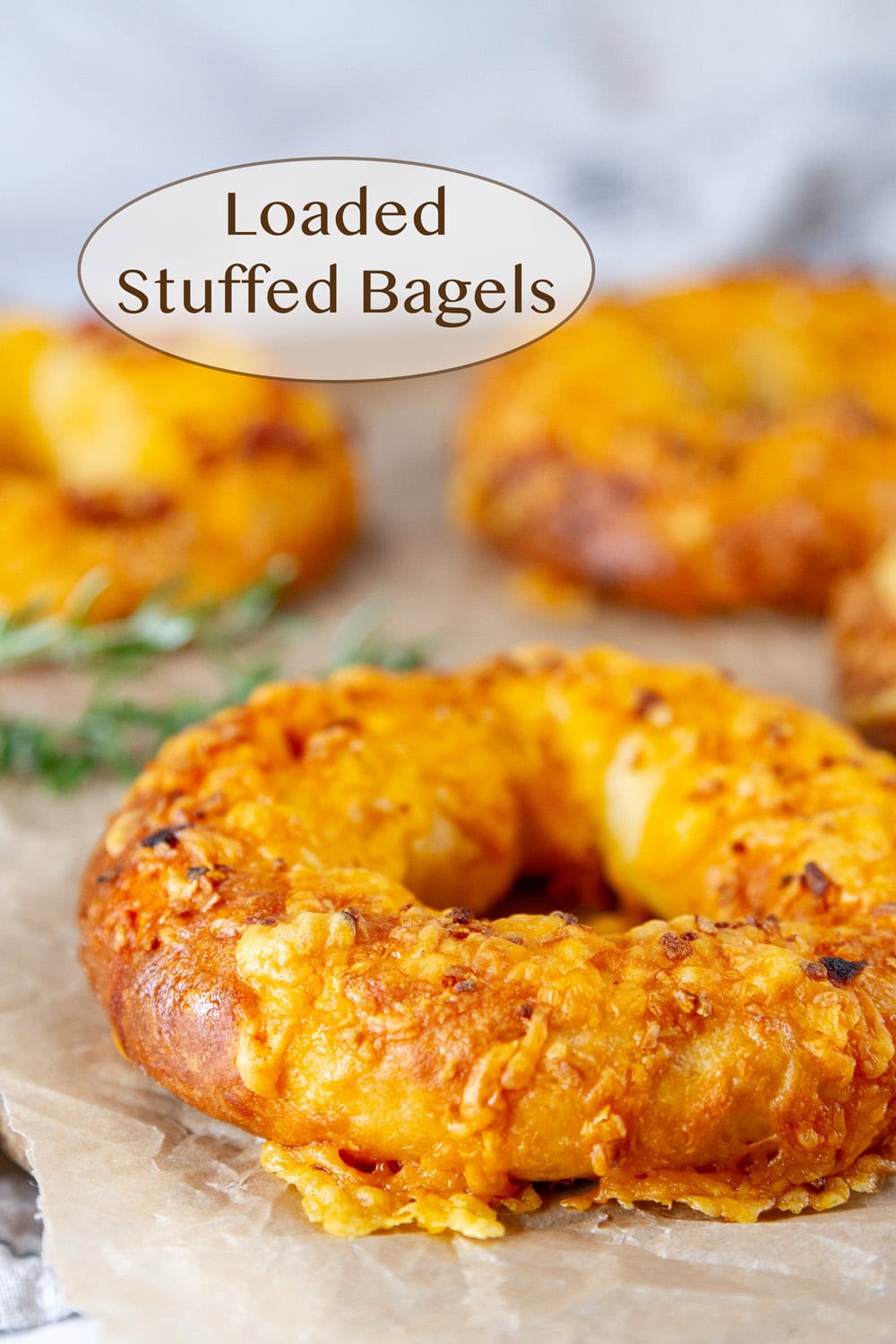 bagels topped with cheddar cheese on parchment paper with fresh rosemary in the background.