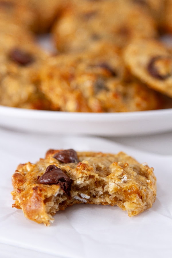 a cookie with a bite taken out of it in front of a plate full of cookies.