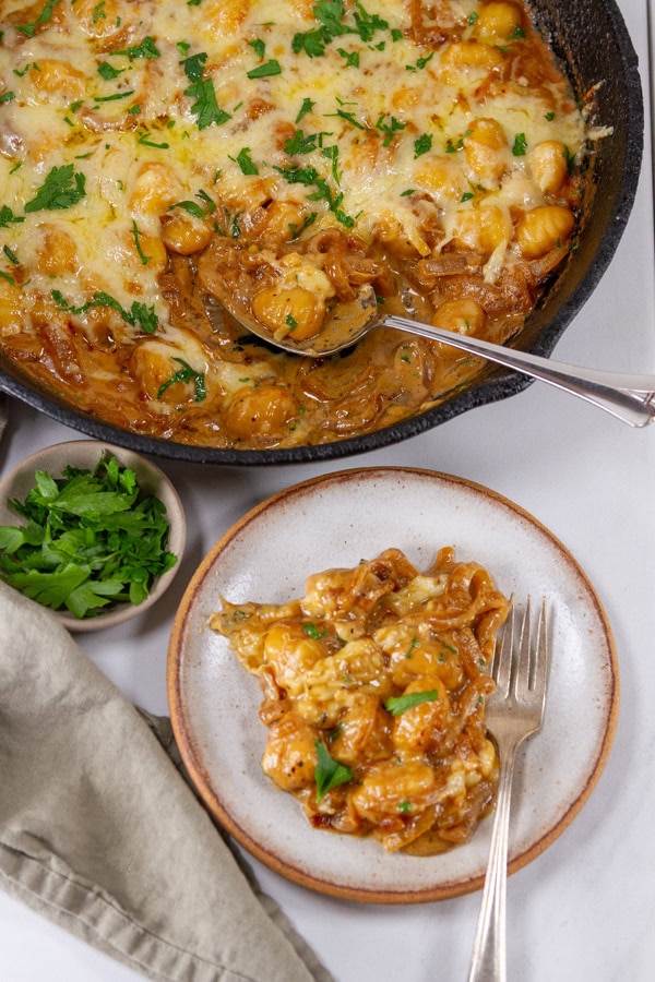 a plate full of gnocchi skillet meal next to the cast iron skillet and a bowl of parsley.