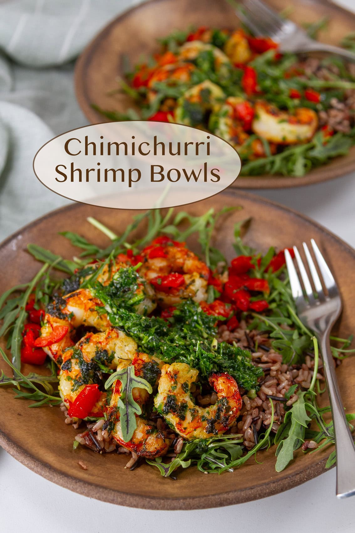 two bowls of shrimp, greens, veggies, and grains with a fork on the right side.
