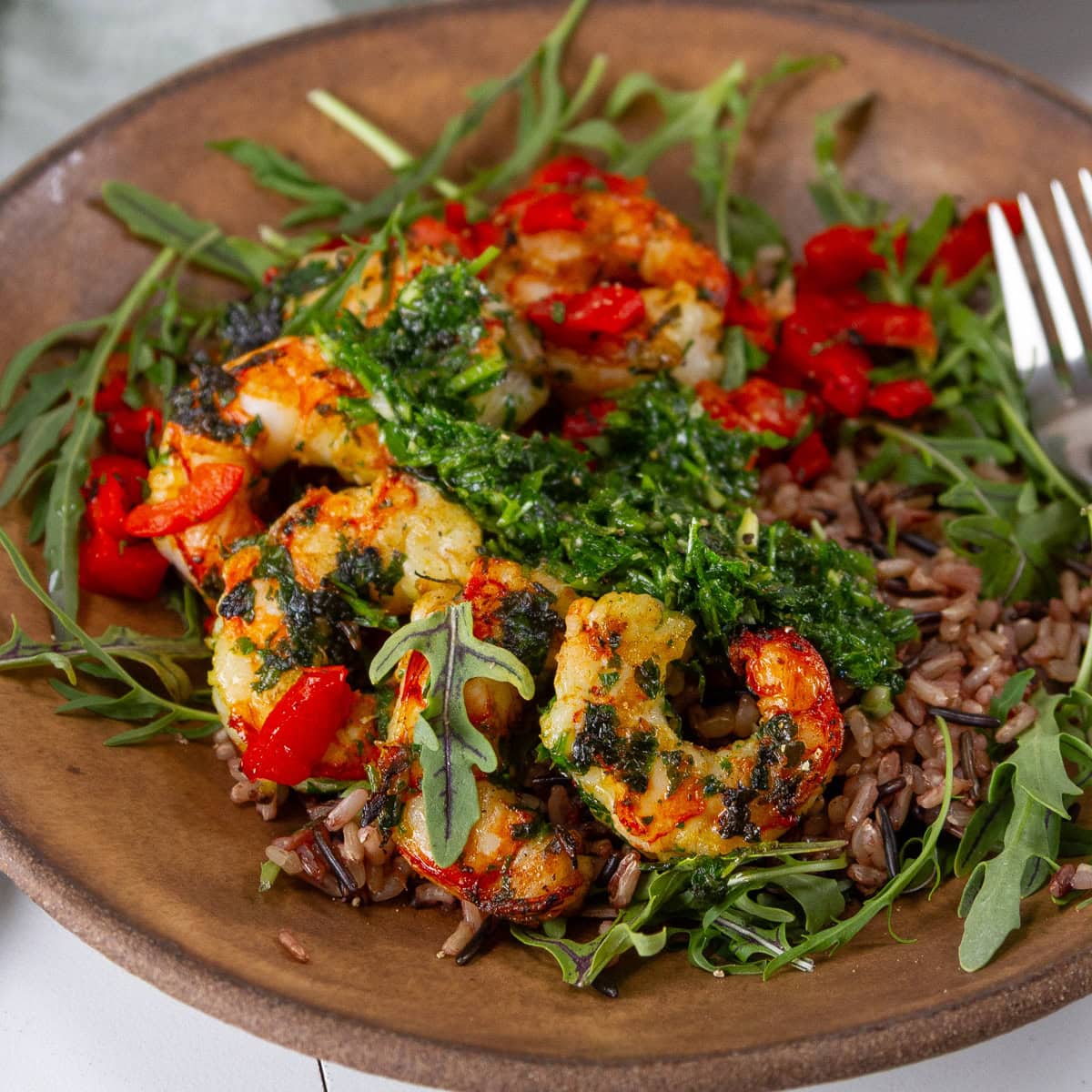 square crop of a brown bowl filled with rice, veggies, and shrimp and a fork on the right side.