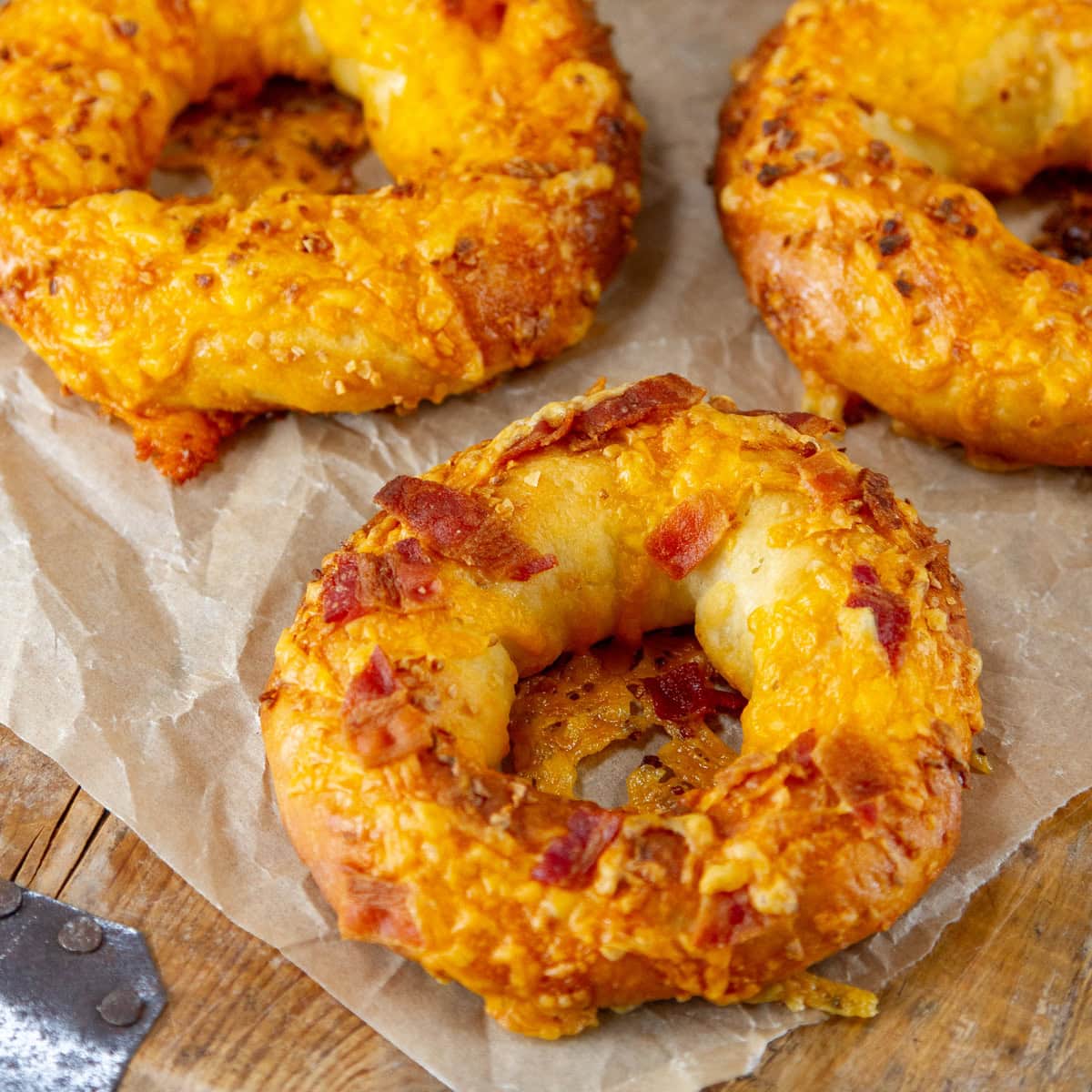 square crop of bagels covered with baked on cheddar cheese and bacon pieces.