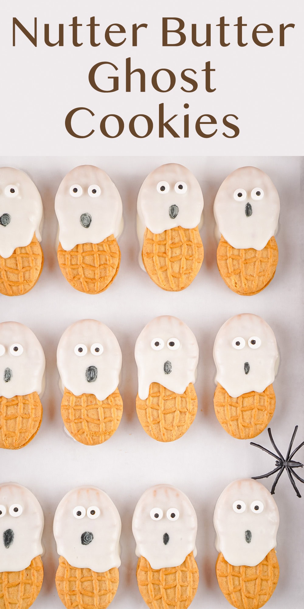 ghost cookies on a white baking sheet with a plastic spider.