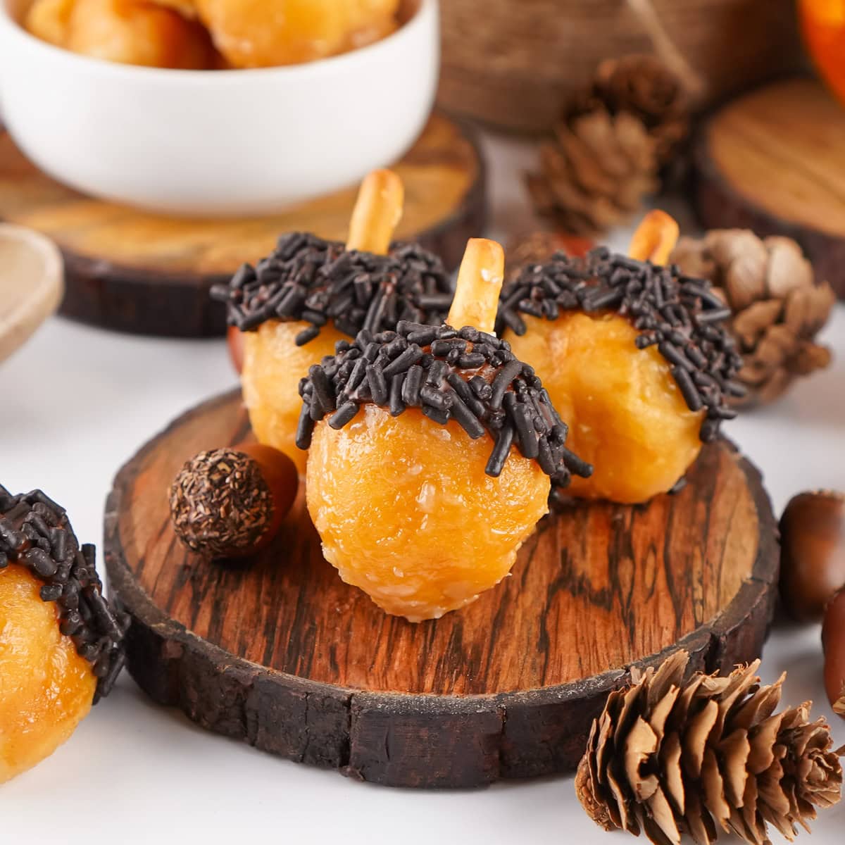 square crop of acorn donut holes on a wooden plate with fall decor around them.