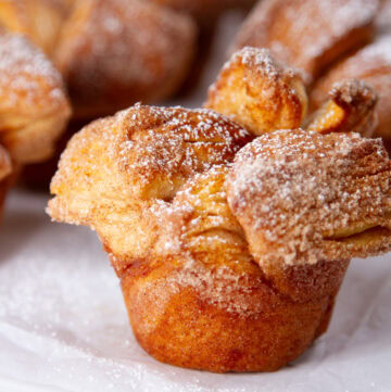 square crop of a cinnamon sugar muffin bun in front of some other buns.
