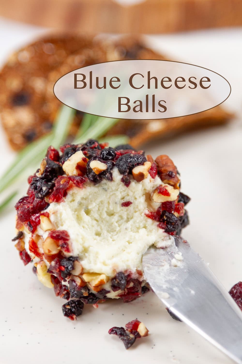 A blue cheese ball coasted with fruits and nuts and a spreader knife in it.