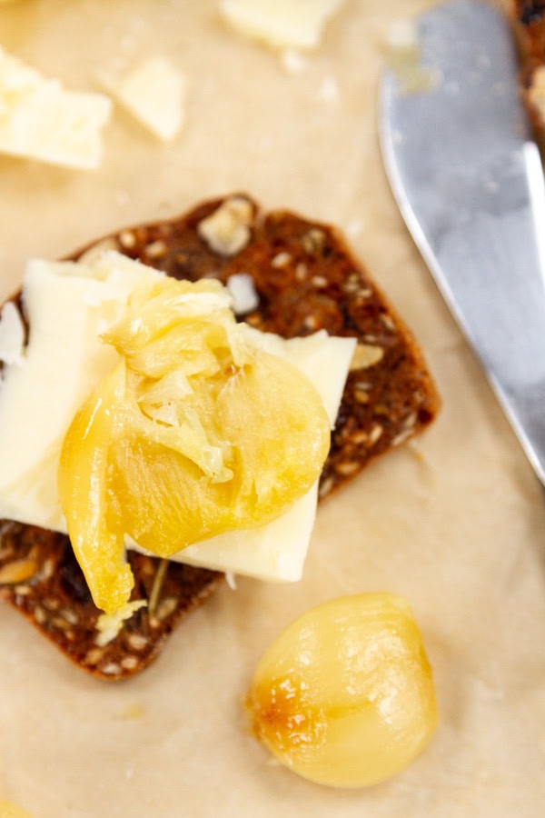 a clove of roasted garlic on a piece of cheese and a cracker.
