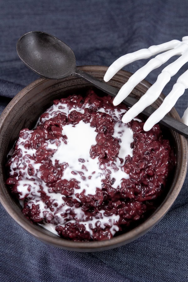 a skeleton hand reaching for a spoon on the side of a bowl of rice pudding.